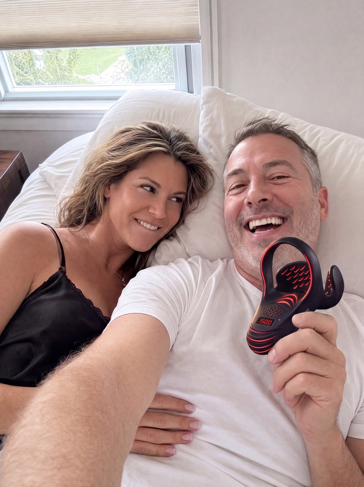 A couple in bed taking a selfie, him laughing and holding PrimePulse