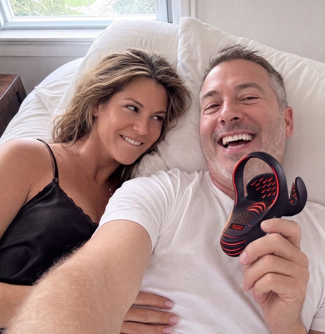A man in his 50s laughing in bed with his wife, holding the PrimePulse device