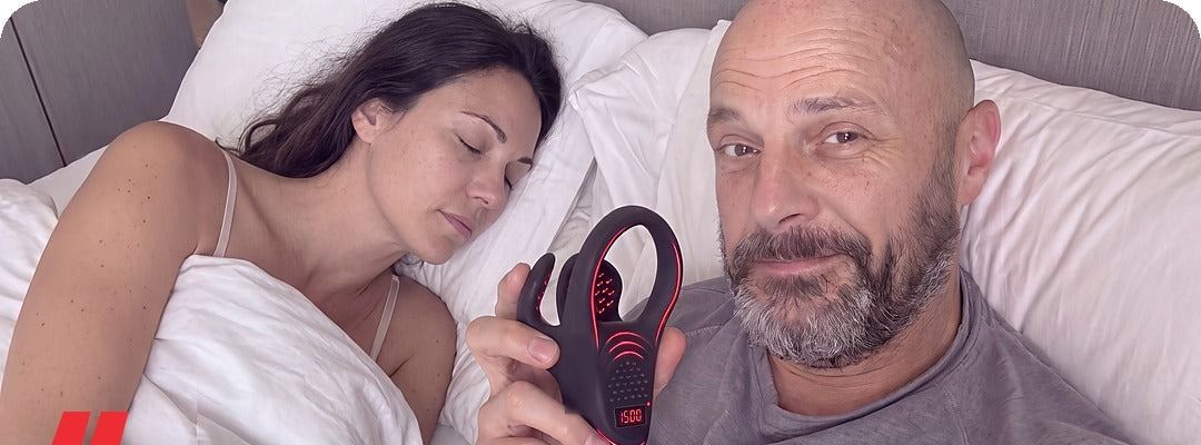 A man in bed holding PrimePulse while his wife sleeps next to him